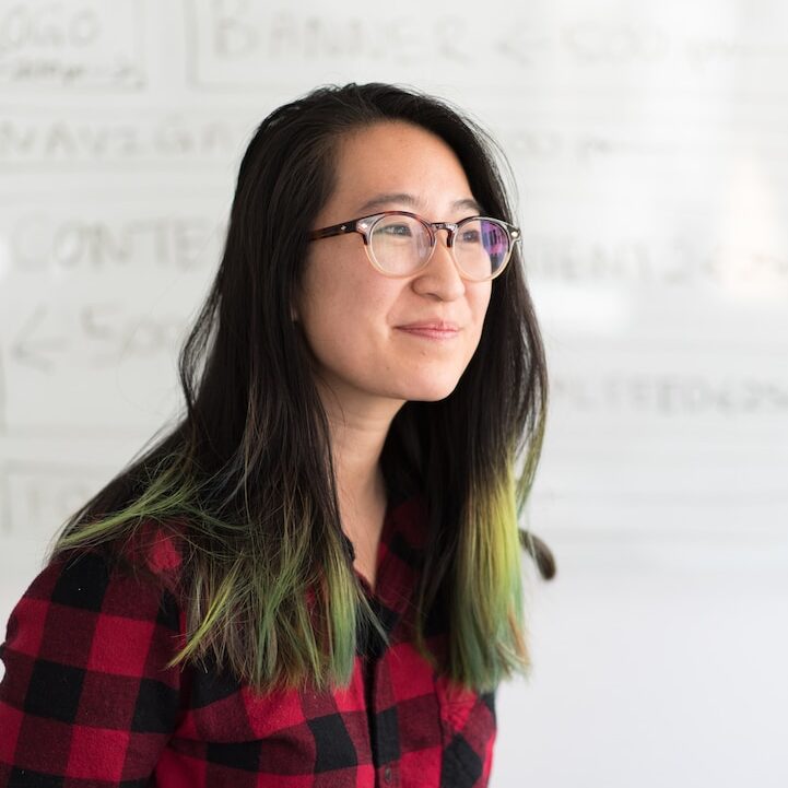 smirking woman wearing red and black checkered top and eyeglasses